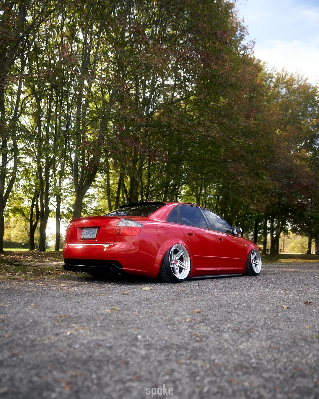 Red Audi parked beneath autumn trees